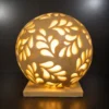 Handcrafted sandstone garden light ball with carved floral pattern glowing warmly on a stone base outdoors