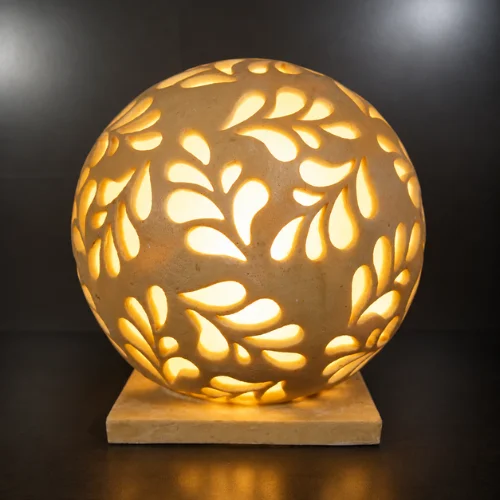 Handcrafted sandstone garden light ball with carved floral pattern glowing warmly on a stone base outdoors