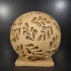 Handcrafted sandstone garden light ball with carved floral pattern glowing warmly on a stone base outdoors