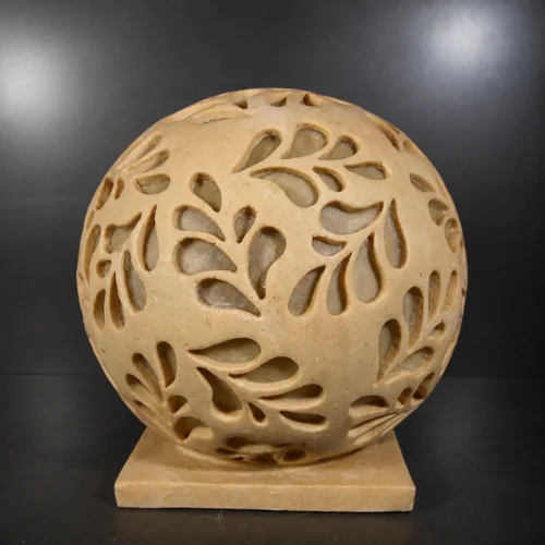 Handcrafted sandstone garden light ball with carved floral pattern glowing warmly on a stone base outdoors