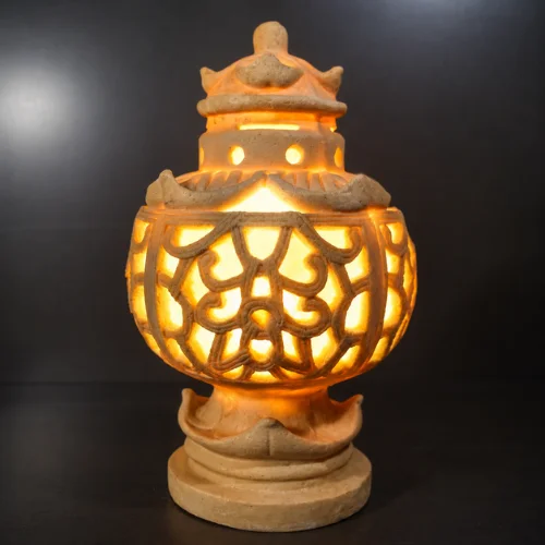 Sandstone garden light ball glowing warm light through carved floral pattern outdoors
