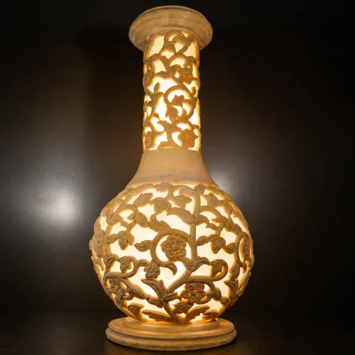 Sandstone flared vase garden light with intricate vine and floral carving and warm glowing illumination